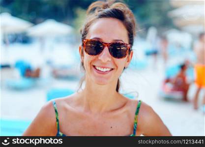 Portrait of young beautiful woman female girl standing on the beach in the sunny summer day wearing sunglasses on the vacation smiling