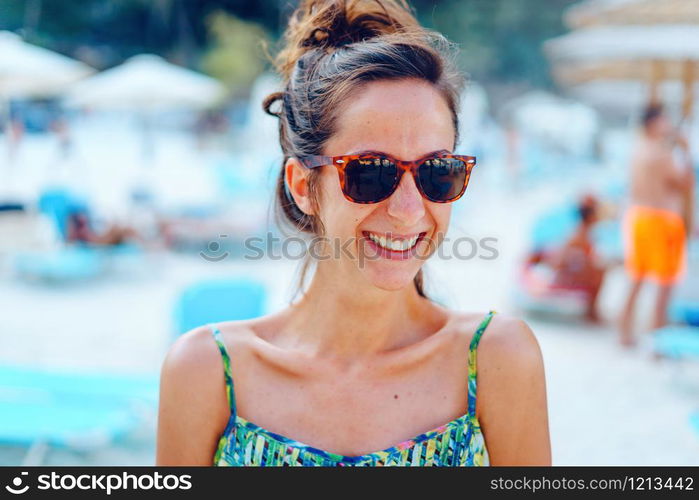 Portrait of young beautiful woman female girl standing on the beach in the sunny summer day wearing sunglasses on the vacation smiling