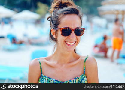 Portrait of young beautiful woman female girl standing on the beach in the sunny summer day wearing sunglasses on the vacation smiling