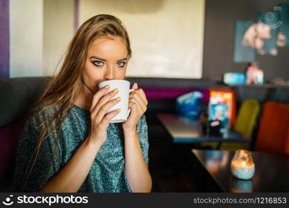 Portrait of young beautiful woman girl sitting alone at cafe having a cup of coffee or tea