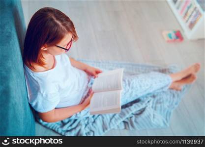 Portrait of young beautiful woman girl student reading or study at home lying on the floor in by the bed wearing glasses holding a book
