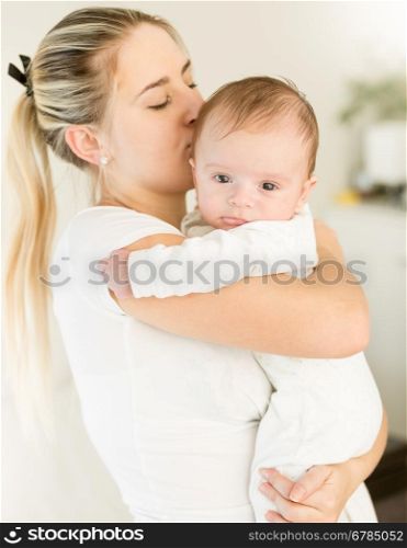 Portrait of young beautiful woman kissing her baby boy on hands