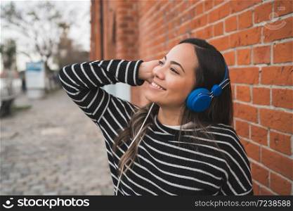 Portrait of young beautiful woman listening to music with blue headphones in the street. Outdoors.