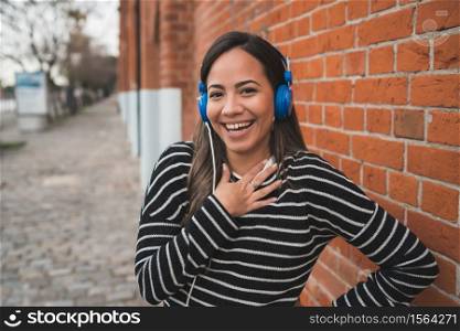 Portrait of young beautiful woman smiling and listening to music with blue headphones in the street. Outdoors.