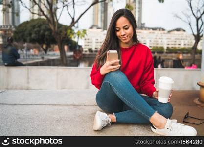 Portrait of young beautiful woman using her mobile phone while sitting outdoors. Communication concept.