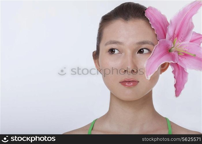 Portrait of young beautiful woman with a large pink flower tucked behind her ear, studio shot