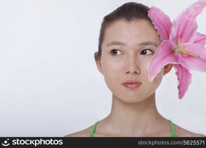 Portrait of young beautiful woman with a large pink flower tucked behind her ear, studio shot
