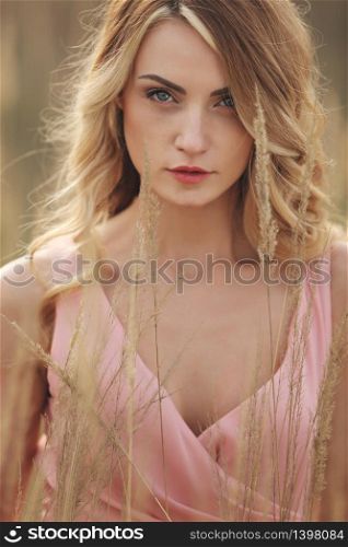 portrait of young beautiful woman with make up outdoors. blond girl with long hair and in a pink dress in field in grass. close up.. portrait of young beautiful woman with make up outdoors. blond girl with long hair and in a pink dress in field in grass. close up
