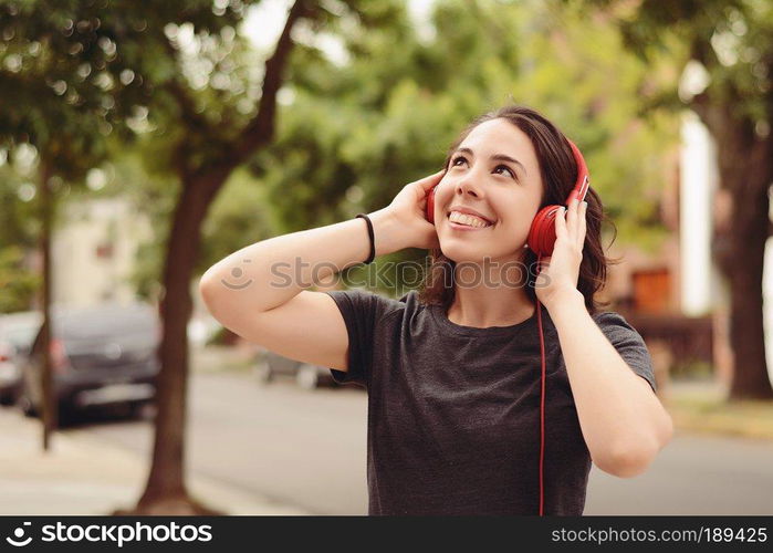 Portrait of young beautiful woman with red headphones listening music. Outdoors. Urban concept.