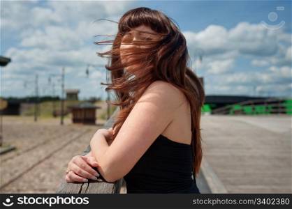 Portrait of young, beautiful woman with wind waving her hair standing on the old-time bridge.