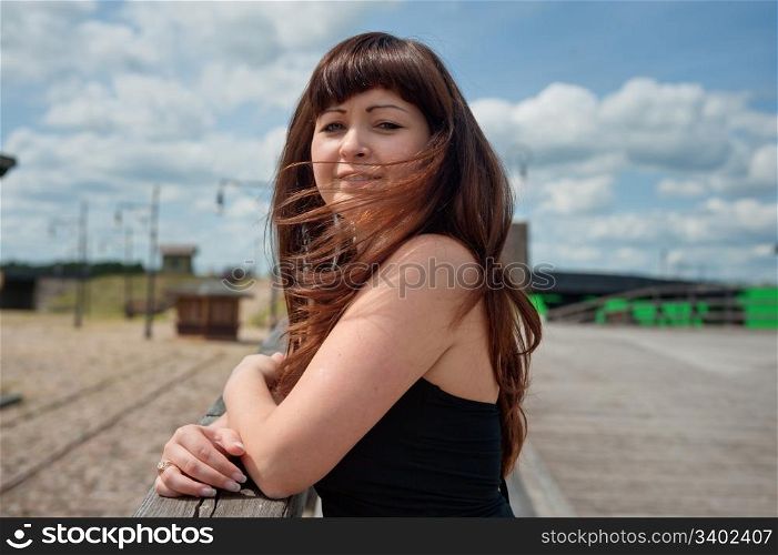 Portrait of young, beautiful woman with wind waving her hair standing on the old-time bridge.
