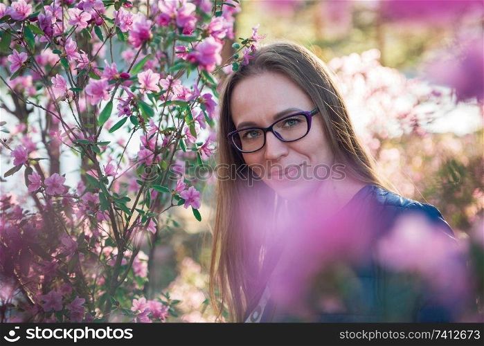 Portrait of young beauty woman in purple rhododendron flowers. Blooming rhododendron - maralnik in Altai mountain forest in the spring.. Blooming maralnik rhododendron in Altai mountains