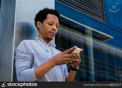 Portrait of young black man typing on his phone. Outdoors.