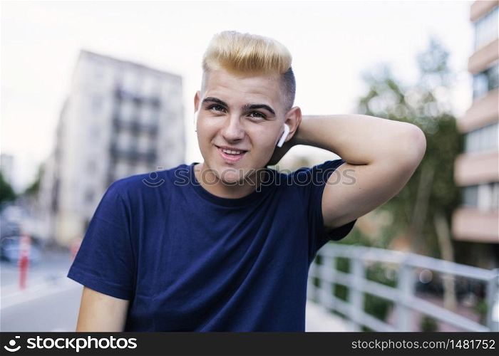 Portrait of young blond male with headphones on the street while looking at the camera