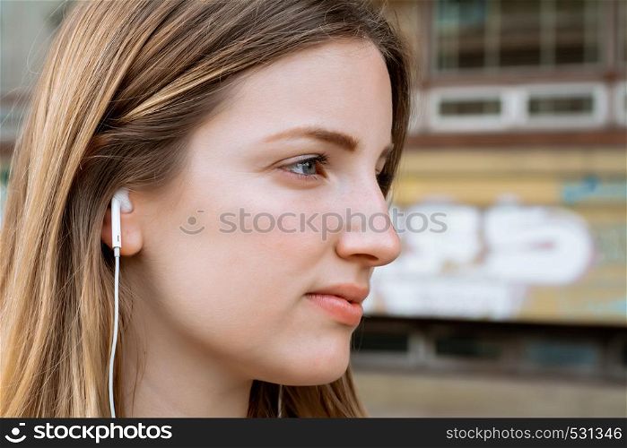 Portrait of young blond woman listening to music with Earphones. Outdoors