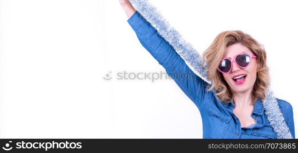 Portrait of young blonde attractive woman in silver tinsel and pink heart shape sunglasses has fun isolated on white background. Merry Christmas and New Year theme. Party time