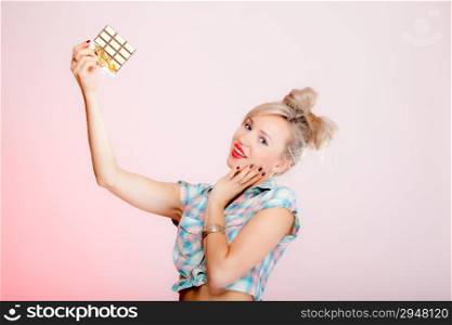 Portrait of young blonde chocolate loving beauty. Sexy girl eating holding chocolate bar on pink background.