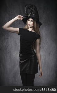 portrait of young blonde female in Halloween day posing with dark style, leather skirt, witch hat and creative make-up