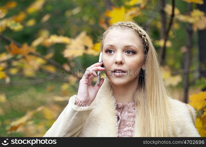 Portrait of young blonde woman talking on mobile phone in autumn park