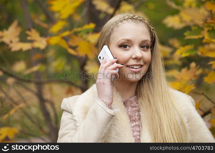 Portrait of young blonde woman talking on mobile phone in autumn park