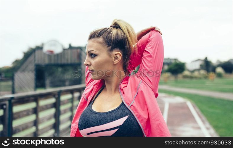 Portrait of young blonde woman with pigtail stretching arms before training outdoors. Young woman stretching arms before training outdoors