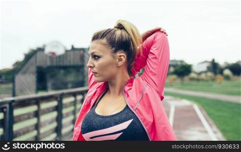 Portrait of young blonde woman with pigtail stretching arms before training outdoors. Young woman stretching arms before training outdoors