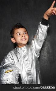 Portrait of young boy (5-6) in astronaut costume pointing upwards smiling studio shot