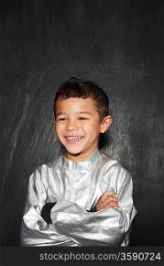 Portrait of young boy (5-6) in silver costume arms crossed smiling studio shot