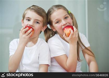 Portrait of young boy and girl in white tshirts eating apples
