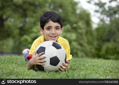 Portrait of young boy lying on grass with ball