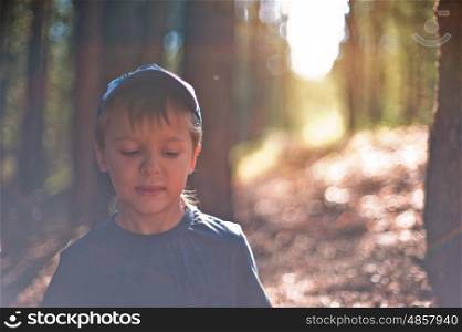 Portrait of young boy sitting in forest. Shallow depth of field.. In the forest