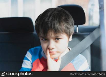 Portrait of young boy with bored face, Kid sad face sitting in the back passenger seat with a safety belt, Unhappy child looking out, Spoiled children concept