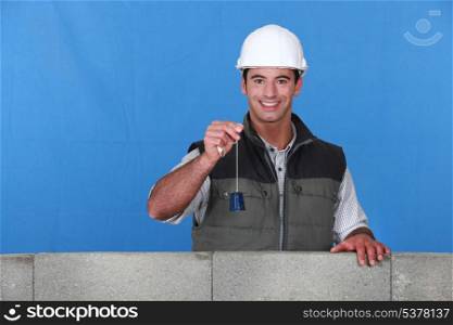 portrait of young bricklayer posing near unfinished concrete wall holding bell