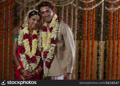 Portrait of young bride and groom wearing garlands during traditional Indian wedding