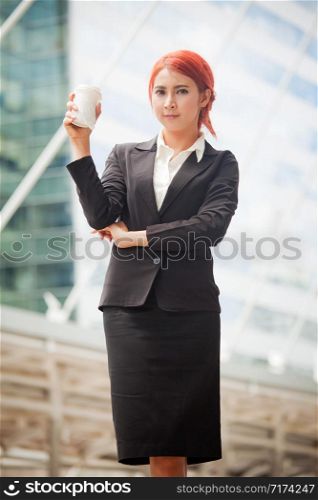 Portrait of young business asian woman standing and smiling with coffee in modern city