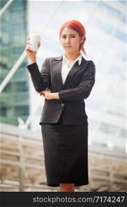 Portrait of young business asian woman standing and smiling with coffee in modern city