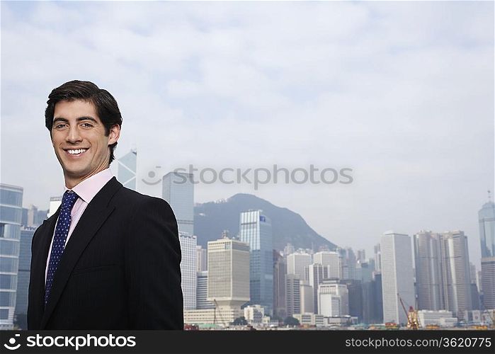 Portrait of young business man smiling, office buildings in background