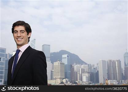 Portrait of young business man smiling, office buildings in background
