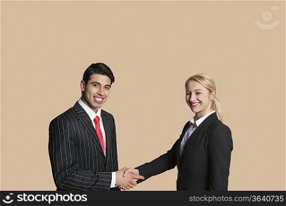 Portrait of young business people shaking hands over colored background