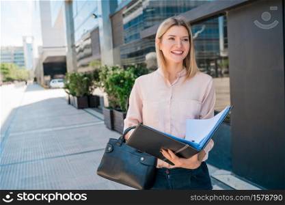 Portrait of young business woman holding clipboard while standing outdoors at the street. Business concept.