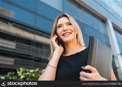 Portrait of young business woman talking on the phone while standing outdoors at the street. Business concept.