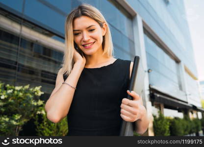 Portrait of young business woman talking on the phone while standing outside office buildings. Business and success concept.