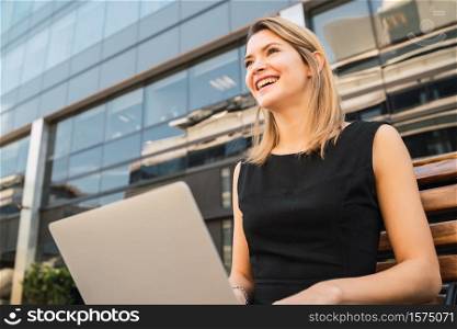 Portrait of young business woman using her laptop while sitting outdoors at the street. Business concept.