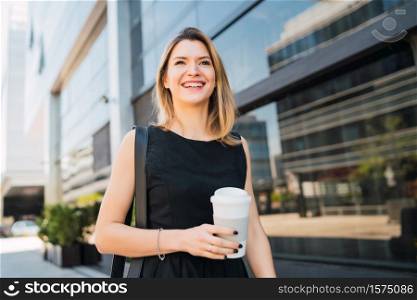 Portrait of young business woman walking to work while drinking takeaway coffee. Business and success concept.