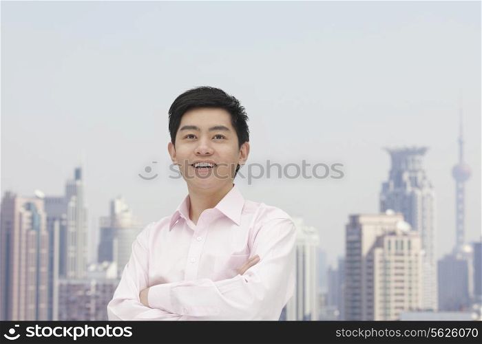 Portrait of young businessman in button down shirt with arms crossed, Shanghai skyline