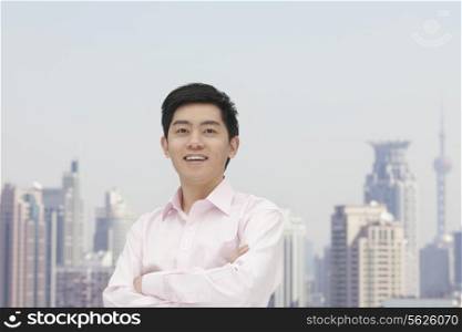 Portrait of young businessman in button down shirt with arms crossed, Shanghai skyline