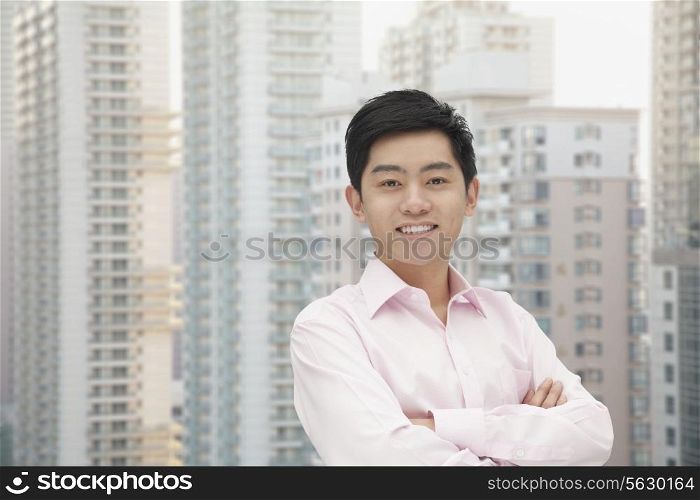 Portrait of young businessman in button down shirt with arms crossed, skyscraper in background