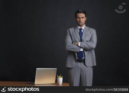 Portrait of young businessman standing arms crossed at office desk