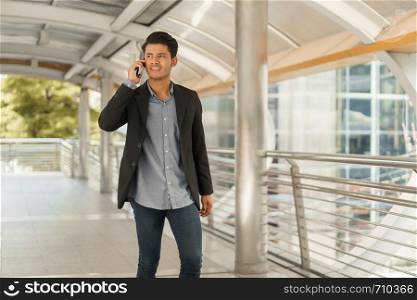 Portrait of young businessman standing at Outside Office and talking on smartphone. Asian Business man wear suit and handsome look.