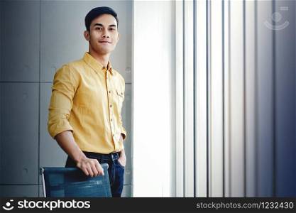 Portrait of Young Businessman Standing by the Window in Office. Looking at Camera and Smiling. Happy Person with Smile Face